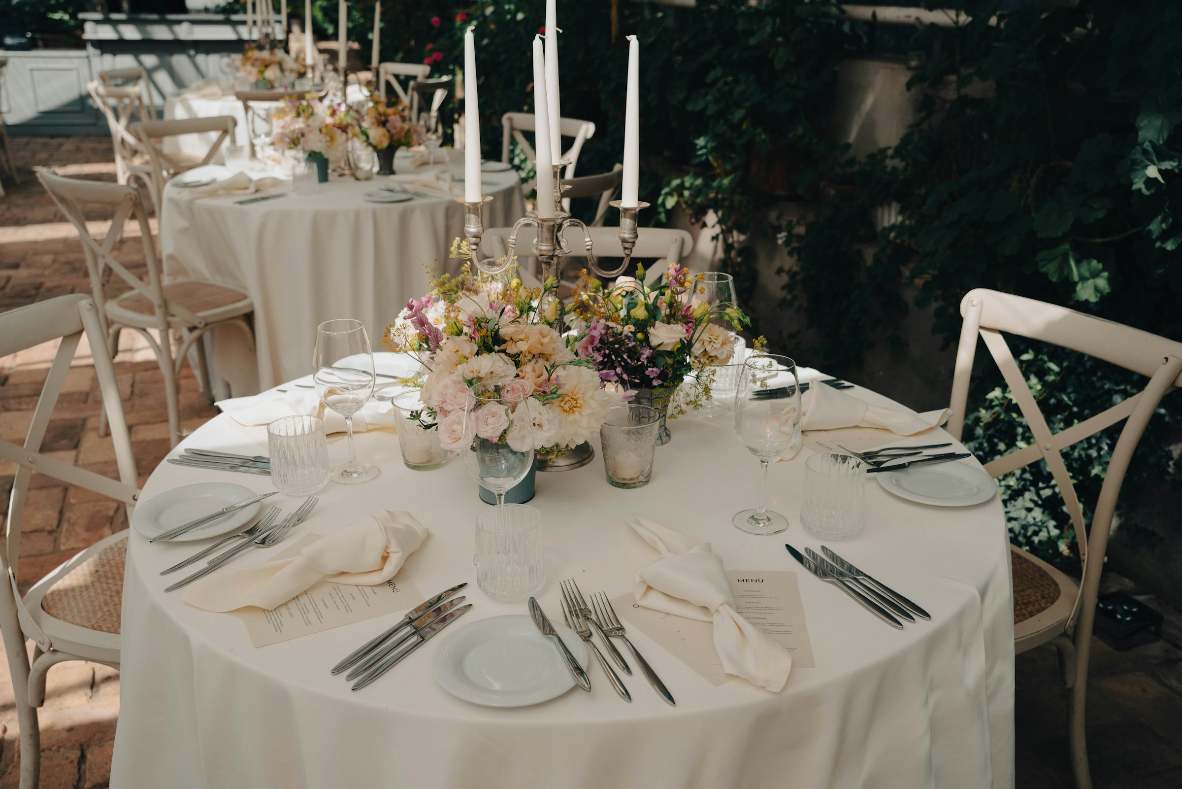 A round wedding table set with tall candles, garden florals and menu cards