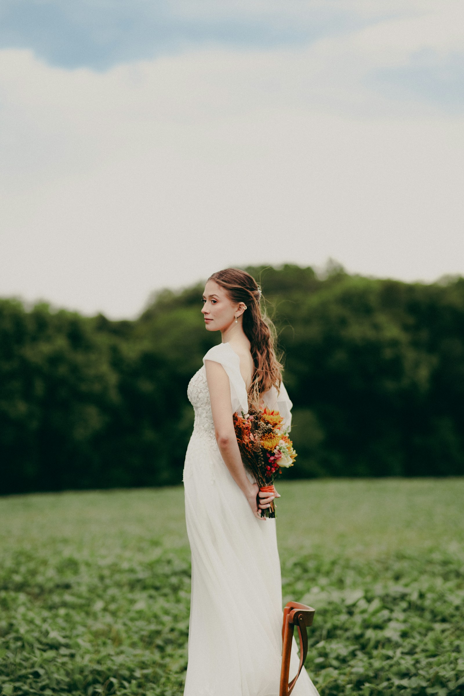 Bride holding an autumn-toned bouquet in an open field