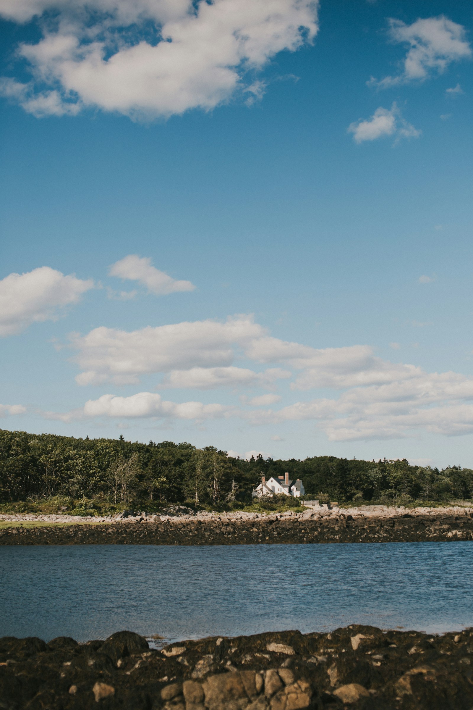 White coastal cottage across the water beneath a wide blue sky