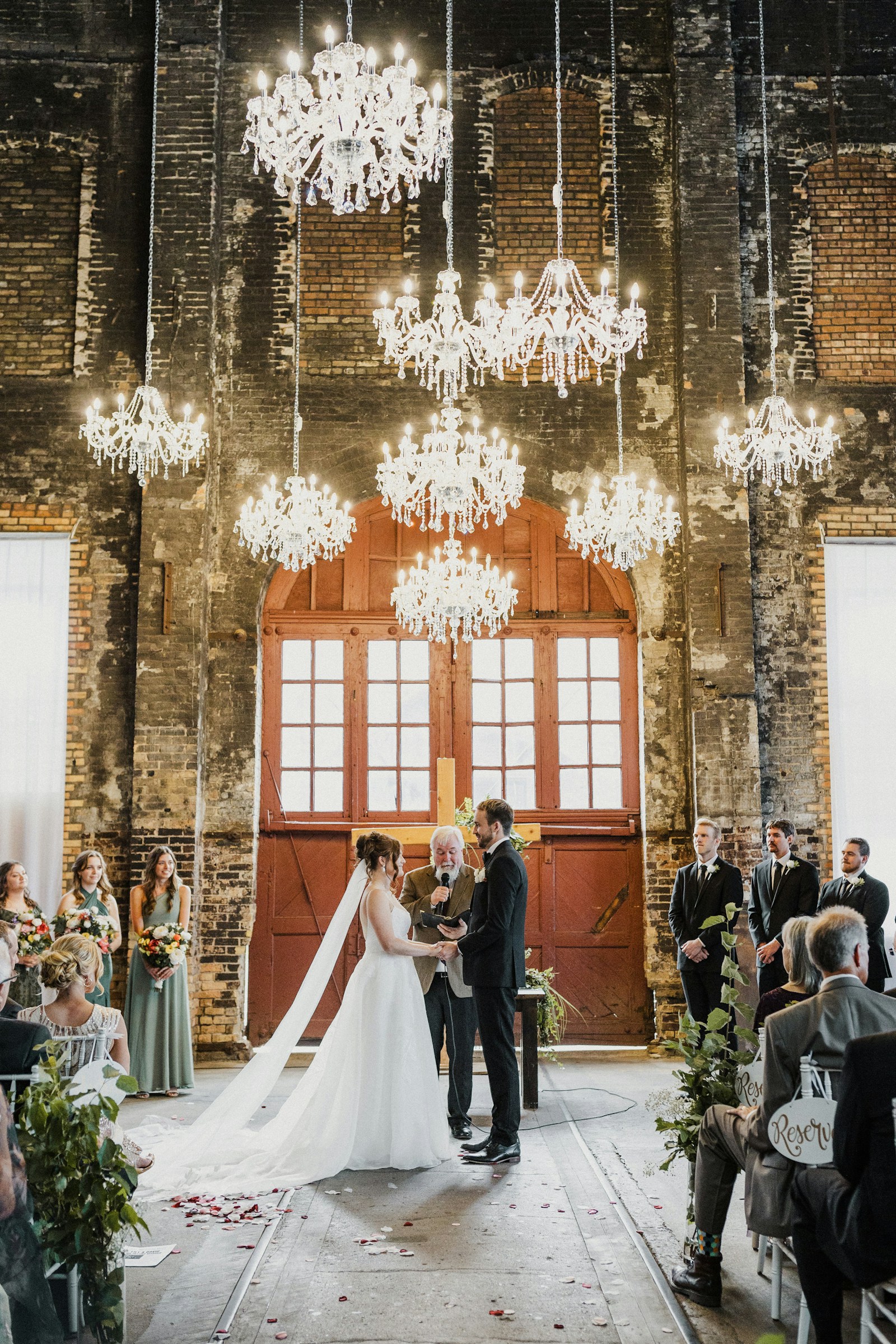 Couple exchanging vows beneath chandeliers in a brick warehouse