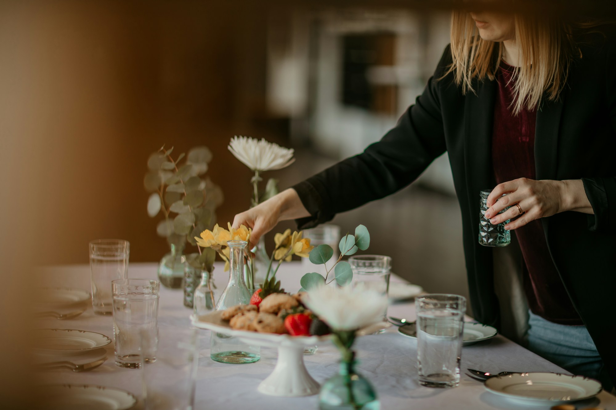 Linden setting glassware on a long table laid with plates and small floral arrangements