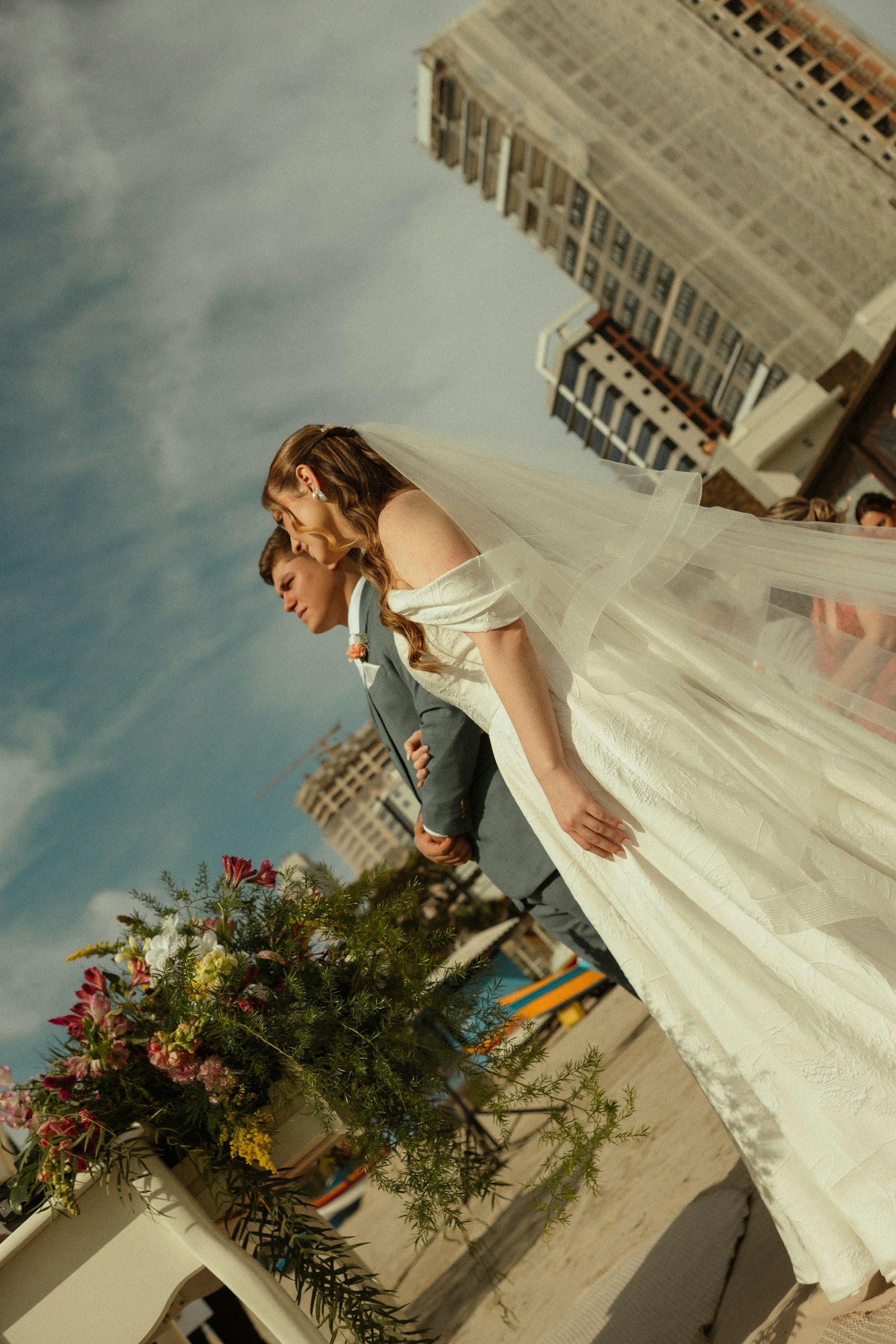 Bride and groom walking past city buildings with her veil lifted by the wind